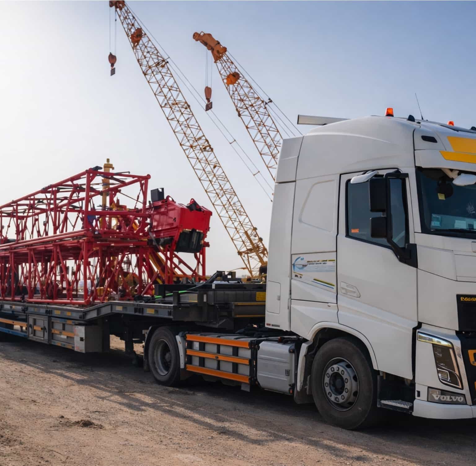White Volvo truck transporting red steel framework with cranes in background