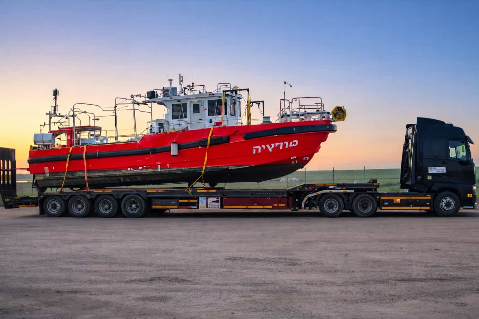 Red vessel being transported on a multi-axle lowbed trailer at sunset